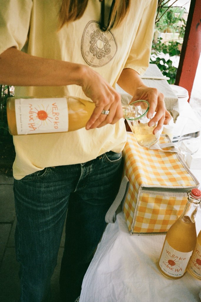 Pouring a bottle of Verokombucha into a glass at a garden table.