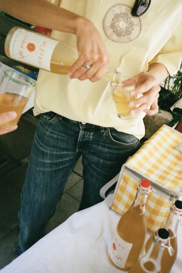 Verokombucha being poured into small glasses beside a gingham cooler bag.