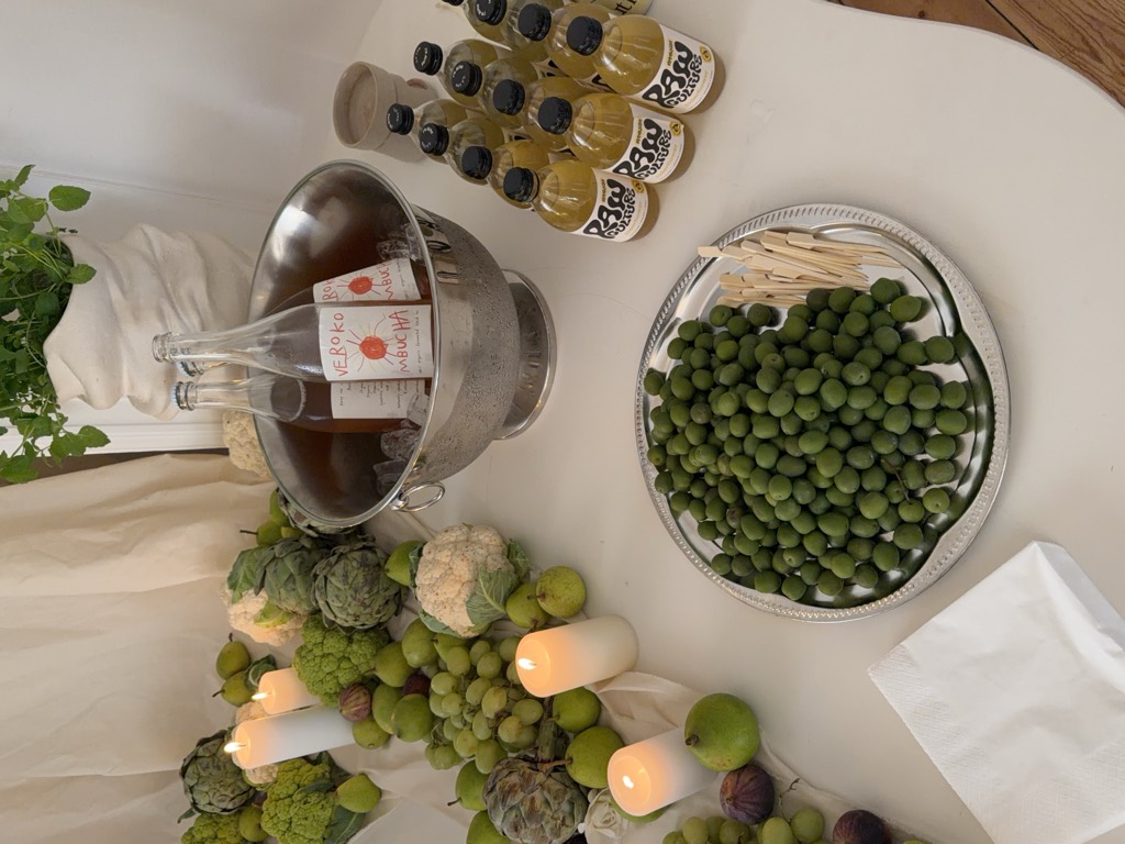 Bottles of Verokombucha on ice at a party table with candles, artichokes and green plums.