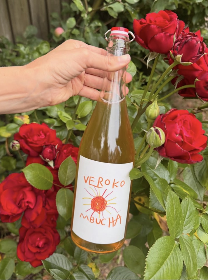 Bottle of Verokombucha held beside red garden roses.